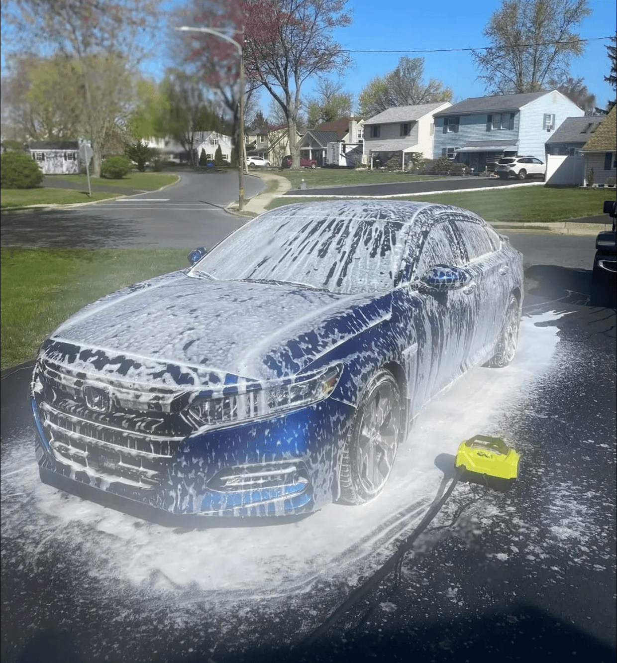 A blue sedan covered in soap foam during a Flawless mobile detail in a residential driveway